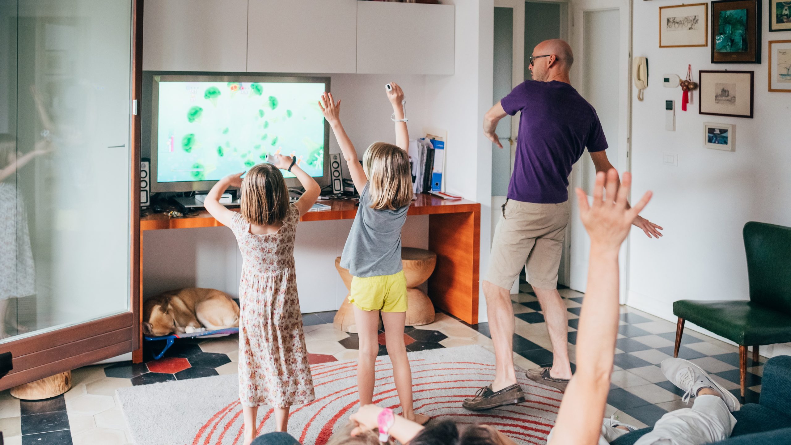 Een familie speelt samen een videogame en danst in de woonkamer