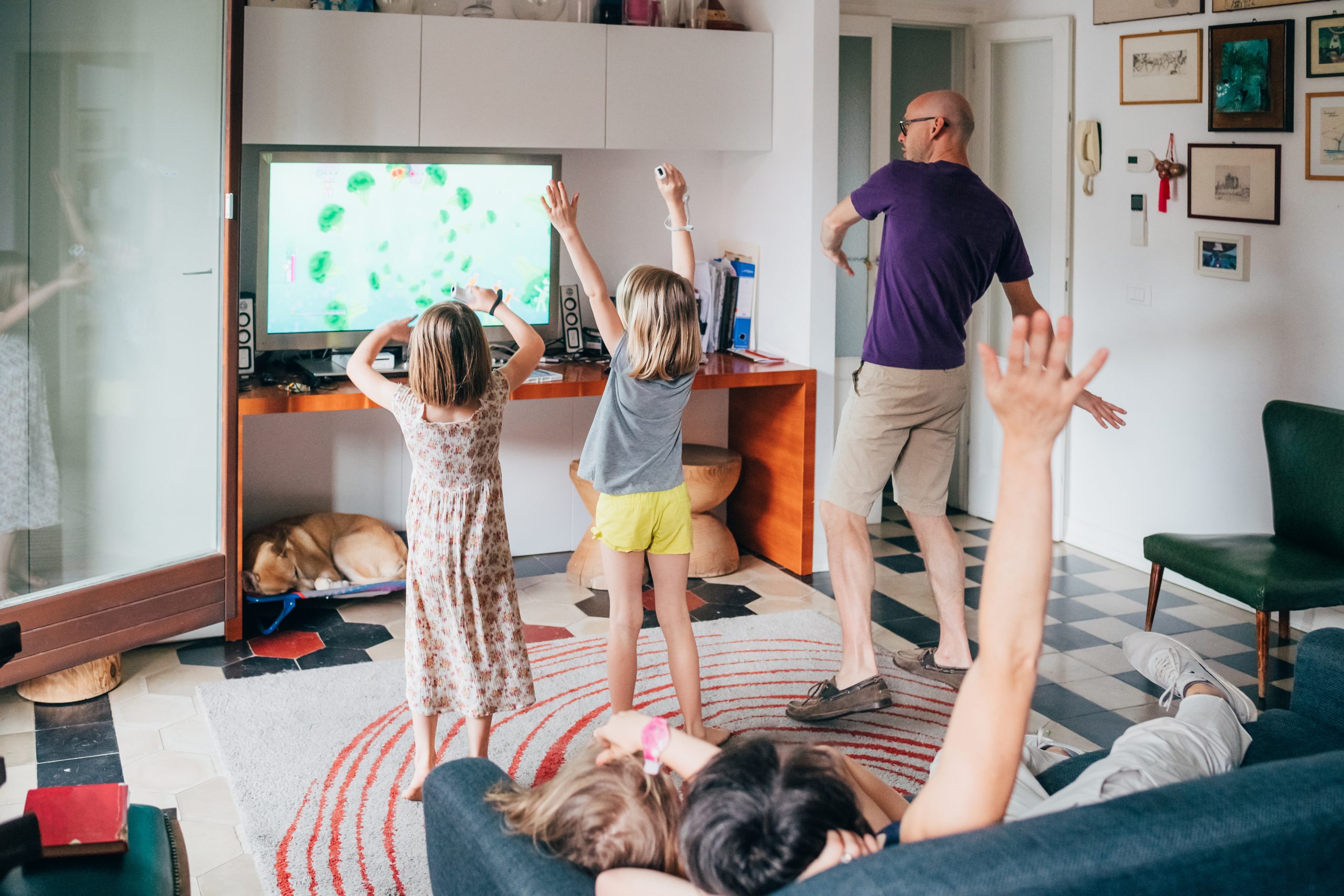 Een familie speelt samen een videogame en danst in de woonkamer
